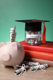 Photo of Piggy bank, graduate hat, books, dollar banknotes and glass jar with word Education on wooden table, closeup. Tuition payment