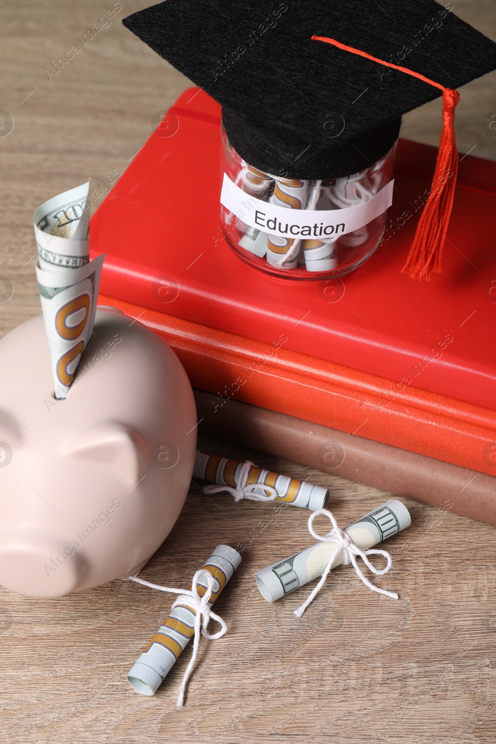 Photo of Piggy bank, graduate hat, books, dollar banknotes and glass jar with word Education on wooden table, closeup. Tuition payment