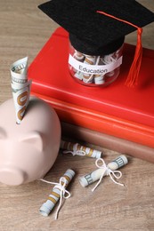 Photo of Piggy bank, graduate hat, books, dollar banknotes and glass jar with word Education on wooden table, closeup. Tuition payment