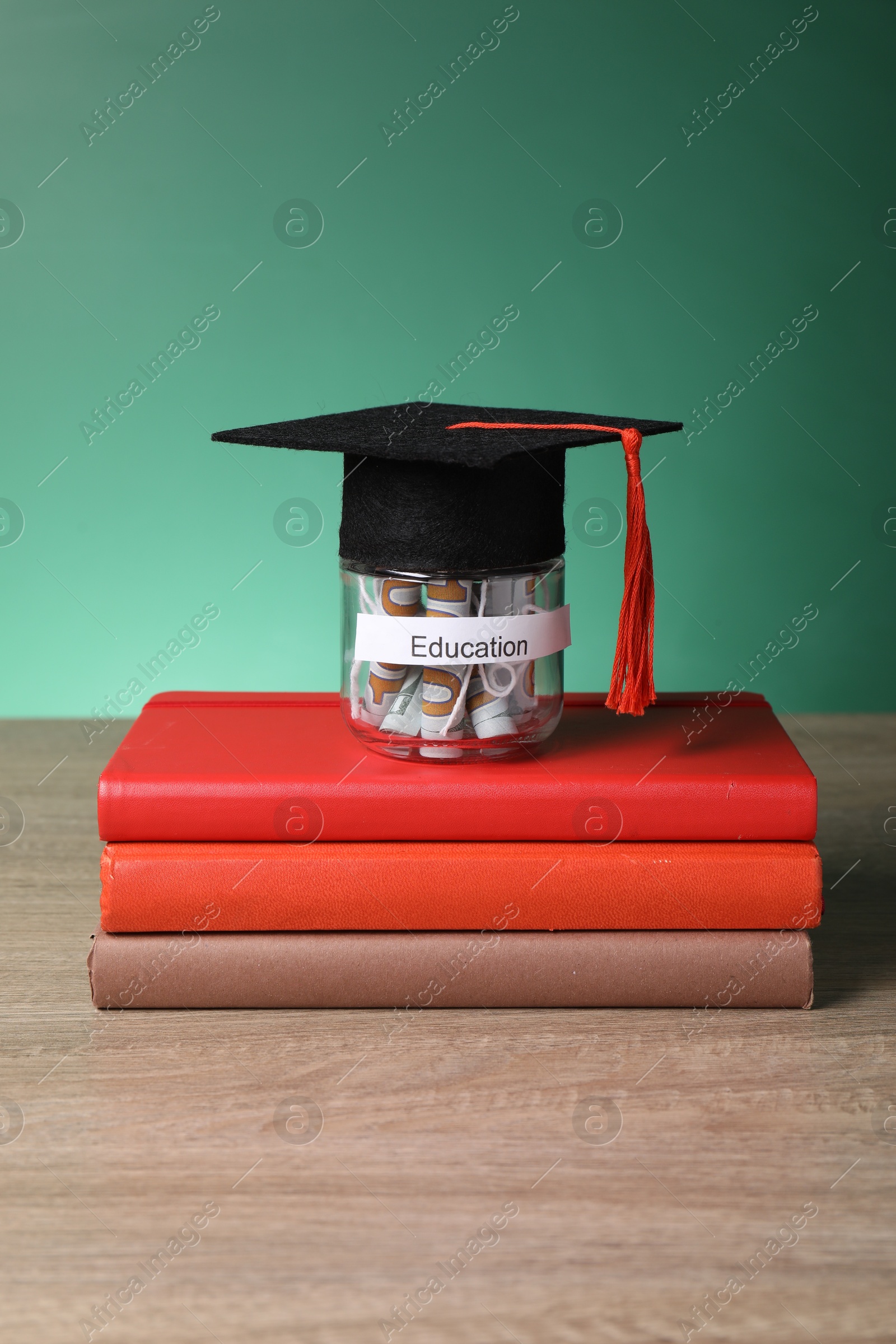 Photo of Graduate hat, books and dollar banknotes in glass jar with word Education on wooden table. Tuition payment