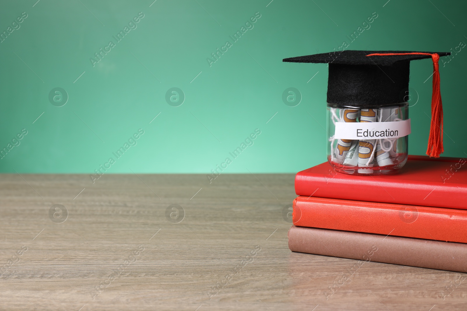 Photo of Graduate hat, books and dollar banknotes in glass jar with word Education on wooden table, space for text. Tuition payment