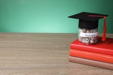 Photo of Graduate hat, books and dollar banknotes in glass jar with word Education on wooden table, space for text. Tuition payment