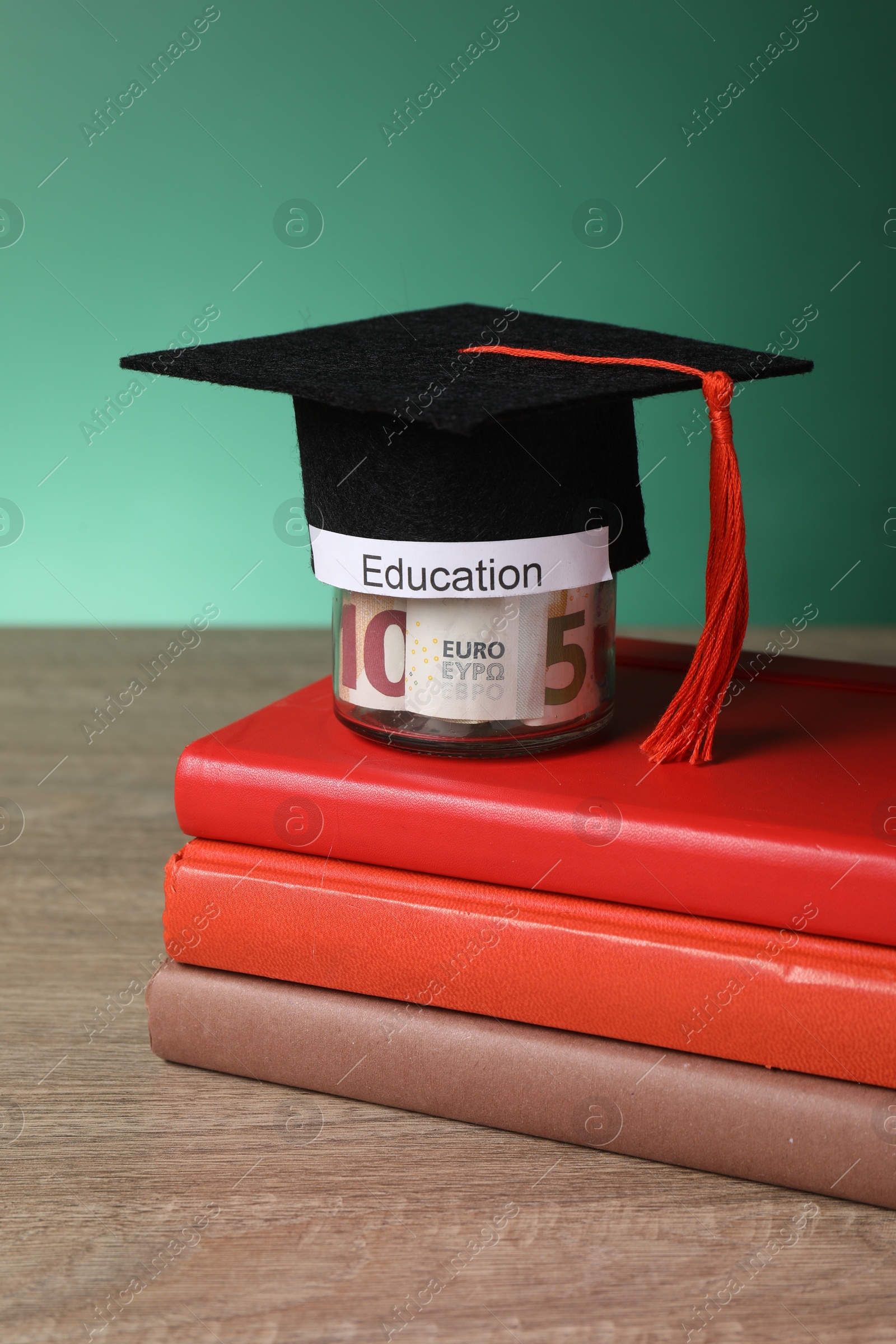 Photo of Graduate hat, books and euro banknotes in glass jar with word Education on wooden table. Tuition payment