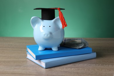 Photo of Graduate hat, piggy bank, dollar banknotes and books on wooden table. Tuition payment