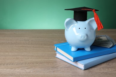 Photo of Graduate hat, piggy bank, dollar banknotes and books on wooden table, space for text. Tuition payment