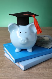 Photo of Graduate hat, piggy bank, dollar banknotes and books on wooden table. Tuition payment