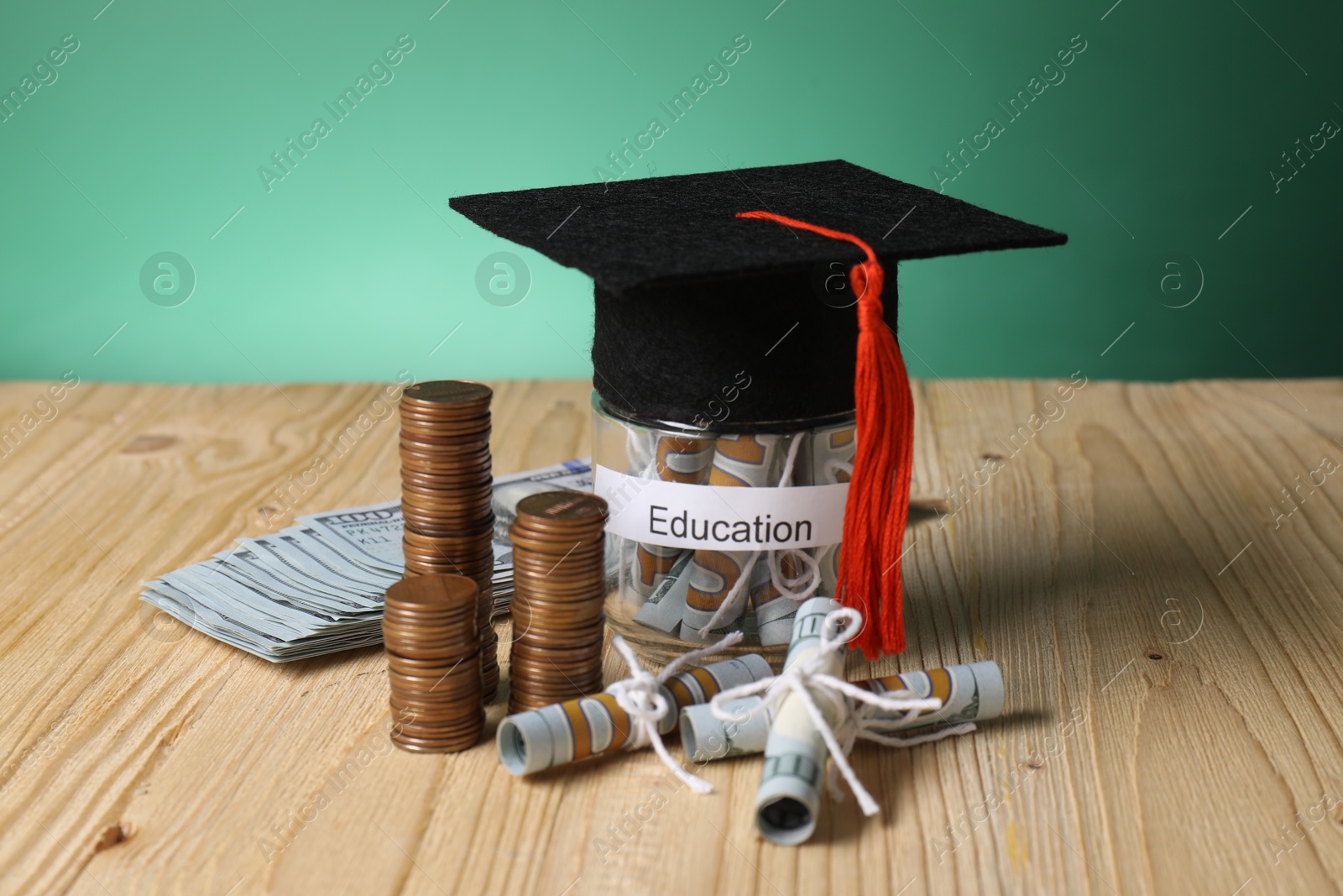 Photo of Graduate hat, dollar banknotes, coins and glass jar with word Education on wooden table. Tuition payment