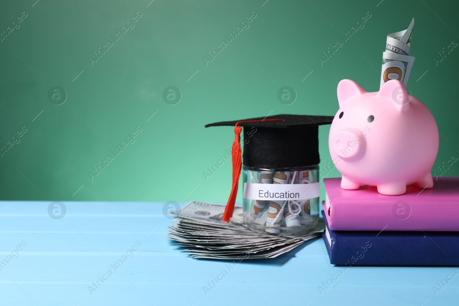 Photo of Piggy bank, graduate hat, books, dollar banknotes and jar with word Education on light blue wooden table, space for text. Tuition payment