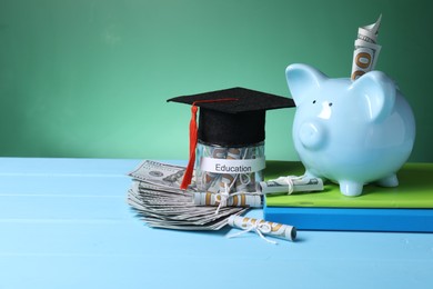 Photo of Piggy bank, graduate hat, books, dollar banknotes and glass jar with word Education on light blue wooden table, space for text. Tuition payment