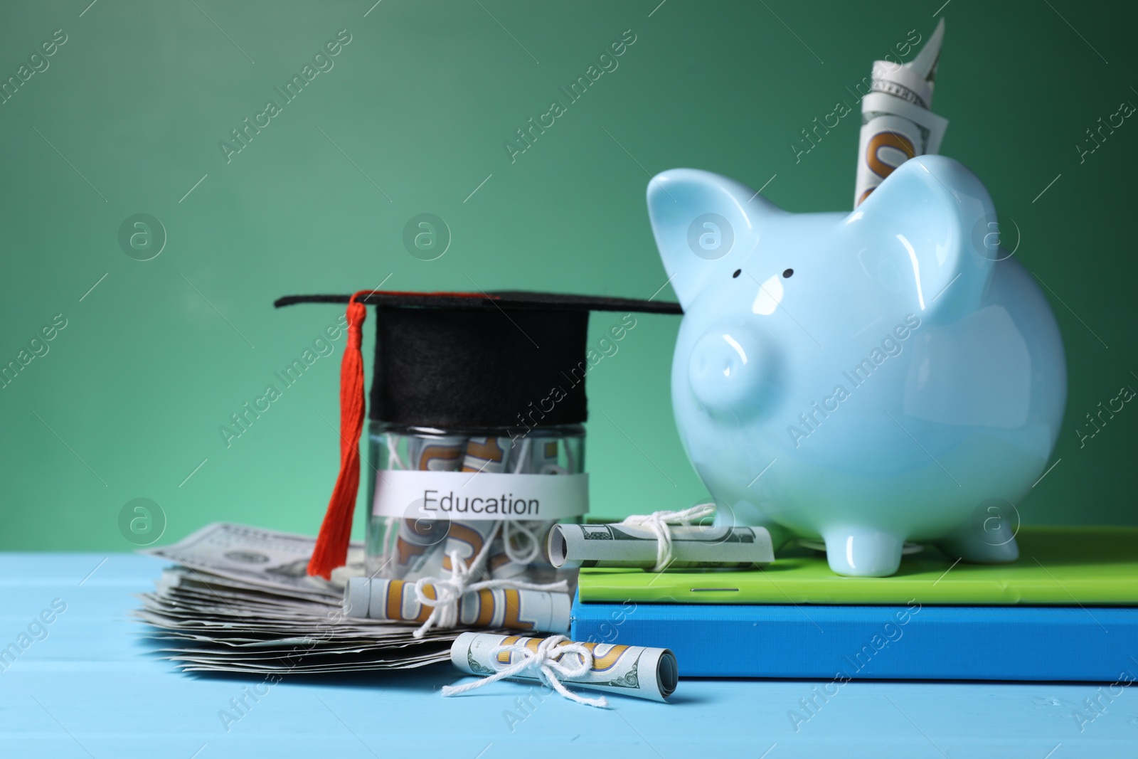 Photo of Piggy bank, graduate hat, books, dollar banknotes and glass jar with word Education on light blue wooden table, closeup. Tuition payment