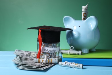 Photo of Piggy bank, graduate hat, books, dollar banknotes and glass jar with word Education on light blue wooden table, closeup. Tuition payment