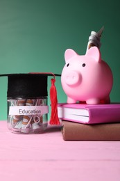 Photo of Piggy bank, graduate hat, books and dollar banknotes in glass jar with word Education on pink wooden table. Tuition payment