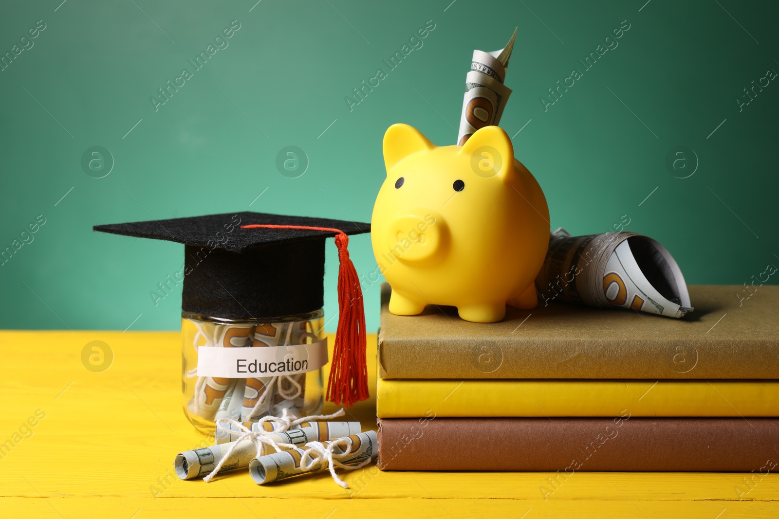 Photo of Piggy bank, graduate hat, books, dollar banknotes and glass jar with word Education on yellow wooden table. Tuition payment