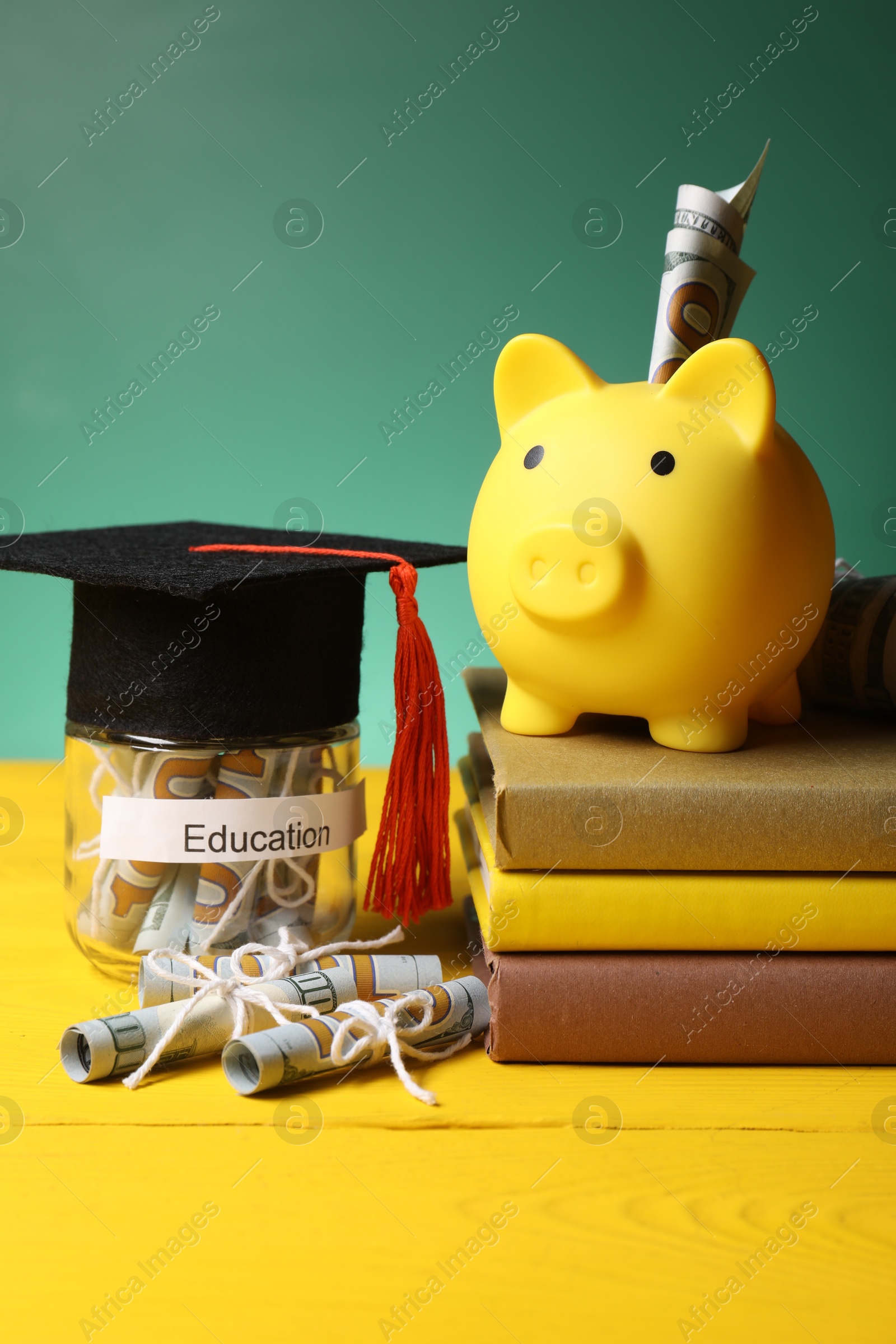 Photo of Piggy bank, graduate hat, books, dollar banknotes and glass jar with word Education on yellow wooden table. Tuition payment