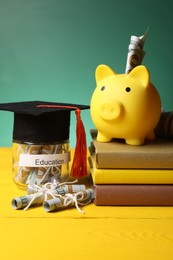 Photo of Piggy bank, graduate hat, books, dollar banknotes and glass jar with word Education on yellow wooden table. Tuition payment