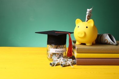 Photo of Piggy bank, graduate hat, books, dollar banknotes and glass jar with word Education on yellow wooden table, space for text. Tuition payment