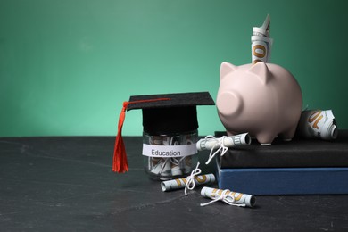 Photo of Piggy bank, graduate hat, books, dollar banknotes and glass jar with word Education on black table, space for text. Tuition payment