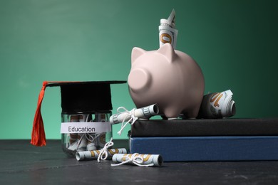 Photo of Piggy bank, graduate hat, books, dollar banknotes and glass jar with word Education on black table. Tuition payment