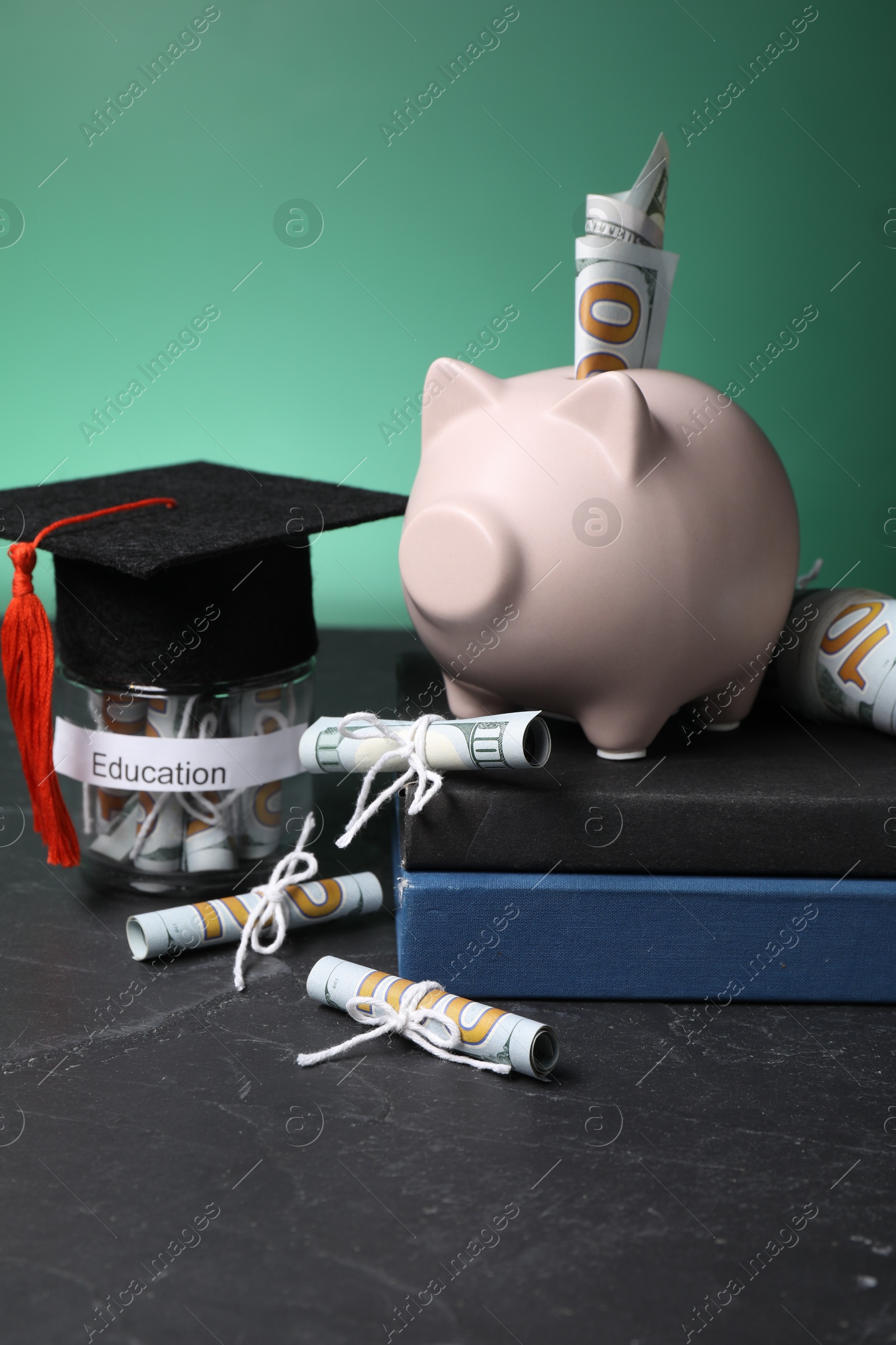 Photo of Piggy bank, graduate hat, books, dollar banknotes and glass jar with word Education on black table. Tuition payment