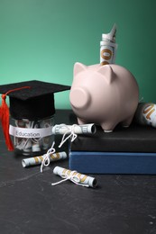 Photo of Piggy bank, graduate hat, books, dollar banknotes and glass jar with word Education on black table. Tuition payment