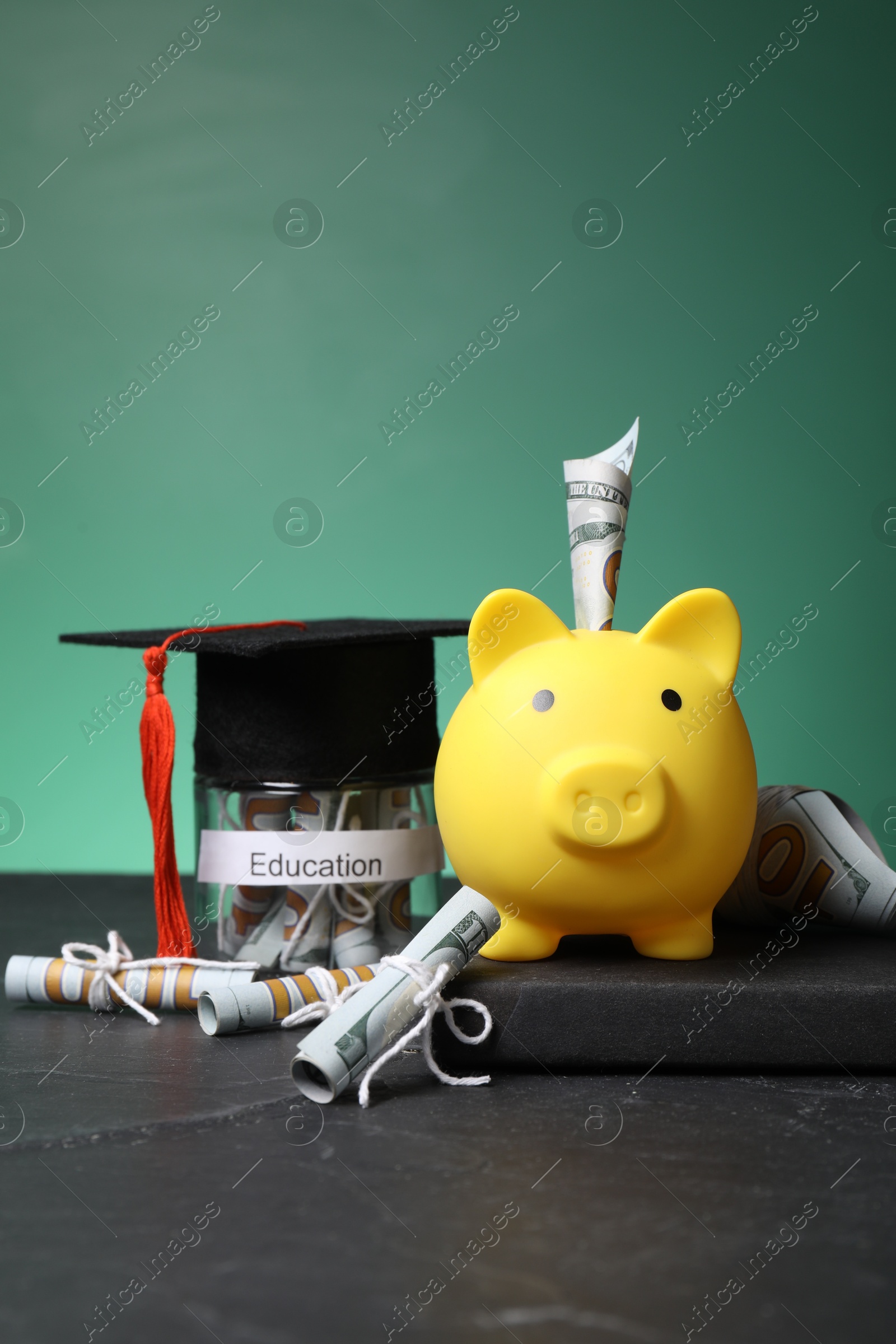 Photo of Piggy bank, graduate hat, book, dollar banknotes and glass jar with word Education on black table. Tuition payment