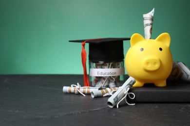 Photo of Piggy bank, graduate hat, book, dollar banknotes and glass jar with word Education on black table, space for text. Tuition payment