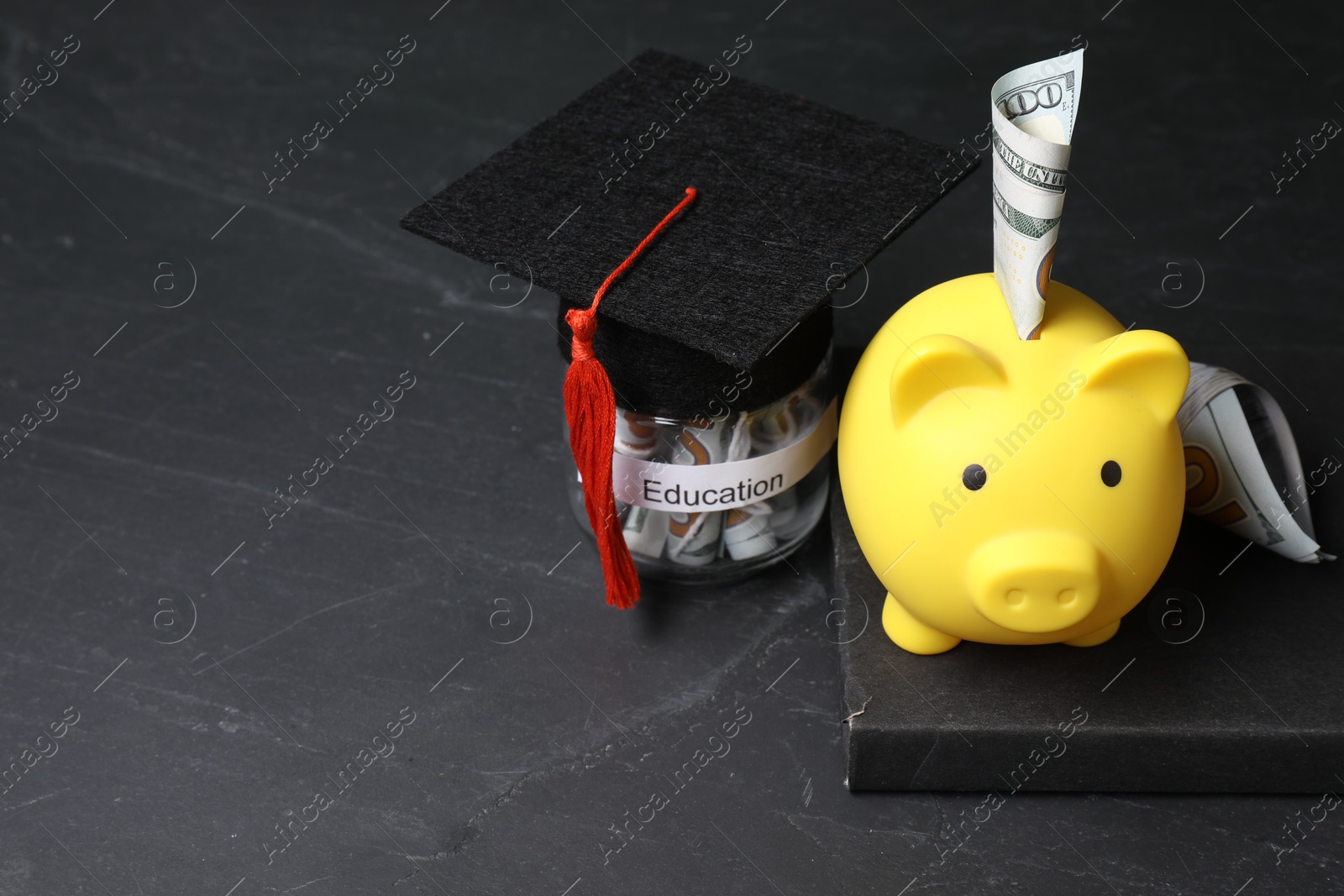 Photo of Tuition payment. Piggy bank, graduate hat, book, dollar banknotes and glass jar with word Education on black table. Space for text