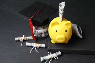 Photo of Piggy bank, graduate hat, book, dollar banknotes and glass jar with word Education on black table. Tuition payment