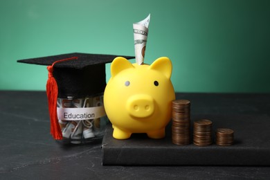 Photo of Piggy bank, graduate hat, coins, book and dollar banknotes in glass jar with word Education on black table. Tuition payment