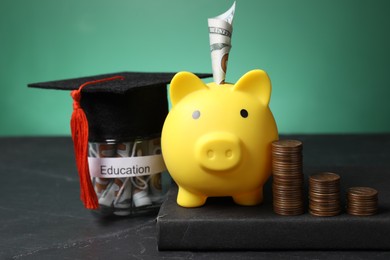 Photo of Piggy bank, graduate hat, coins, book and dollar banknotes in glass jar with word Education on black table, closeup. Tuition payment