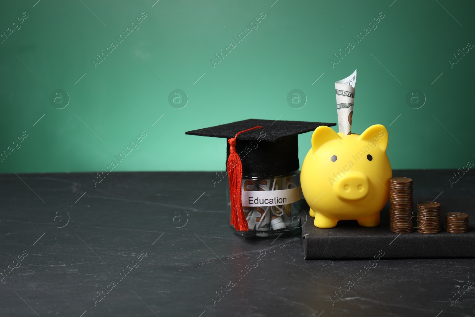 Photo of Piggy bank, graduate hat, coins, book and dollar banknotes in glass jar with word Education on black table, space for text. Tuition payment