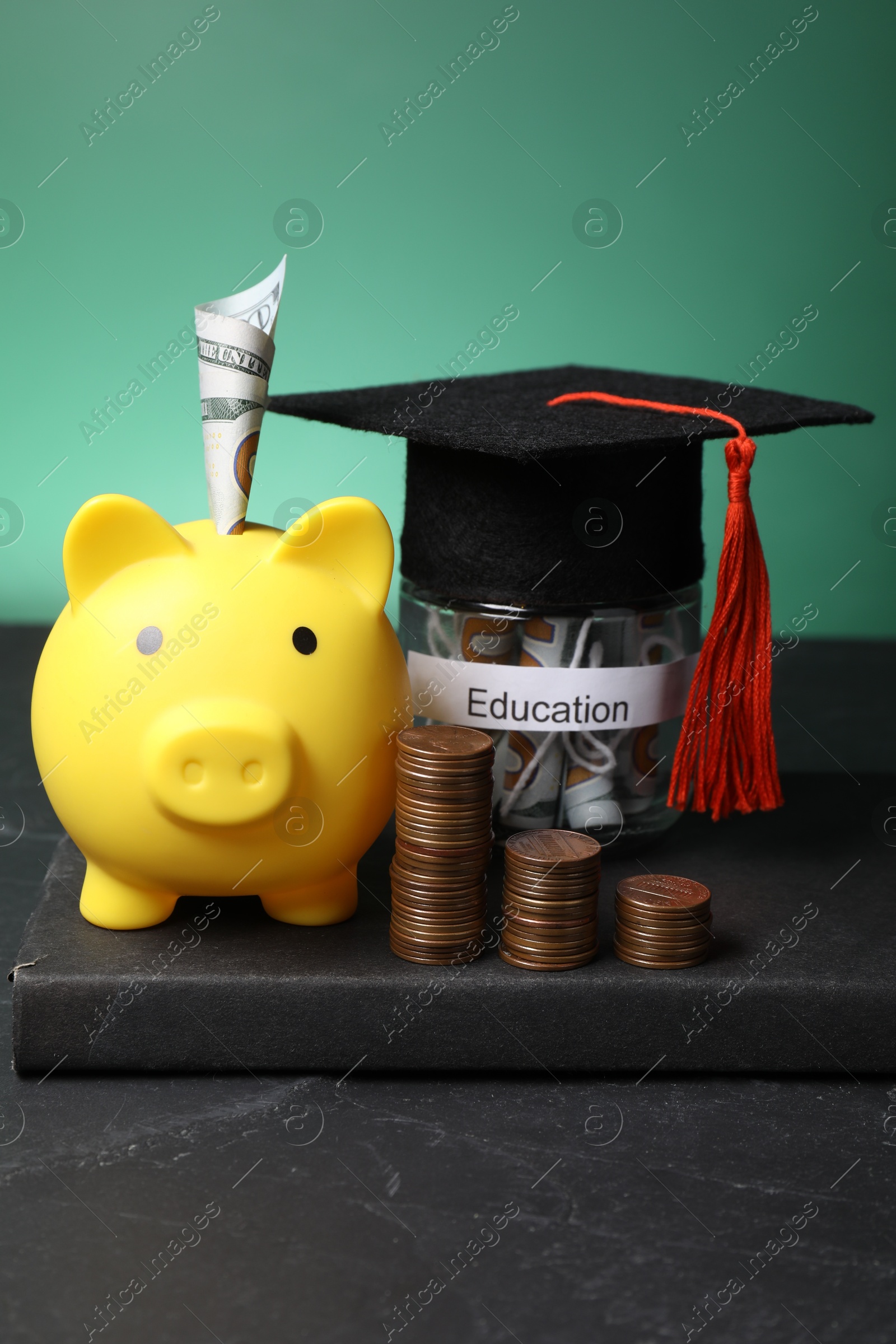 Photo of Piggy bank, graduate hat, coins, book and dollar banknotes in glass jar with word Education on black table. Tuition payment