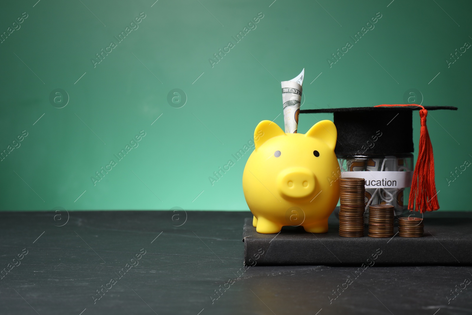 Photo of Piggy bank, graduate hat, coins, book and dollar banknotes on black table, space for text. Tuition payment