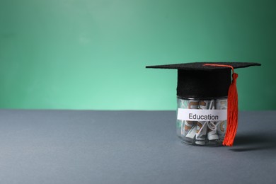 Photo of Graduate hat and dollar banknotes in glass jar with word Education on grey table, space for text. Tuition payment