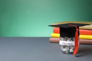 Photo of Tuition payment. Graduate hat, dollar banknotes in glass jar with word Education and books on grey table. Space for text