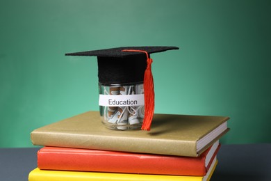 Photo of Graduate hat, dollar banknotes in glass jar with word Education and books on grey table, closeup. Tuition payment