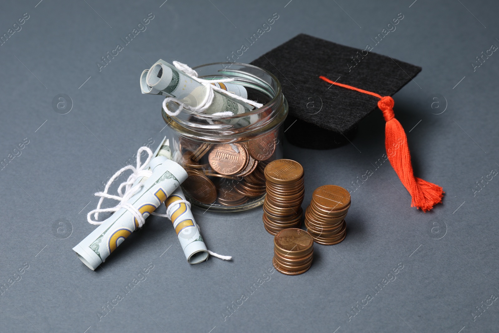 Photo of Dollar banknotes, coins and graduate hat on grey table. Tuition payment