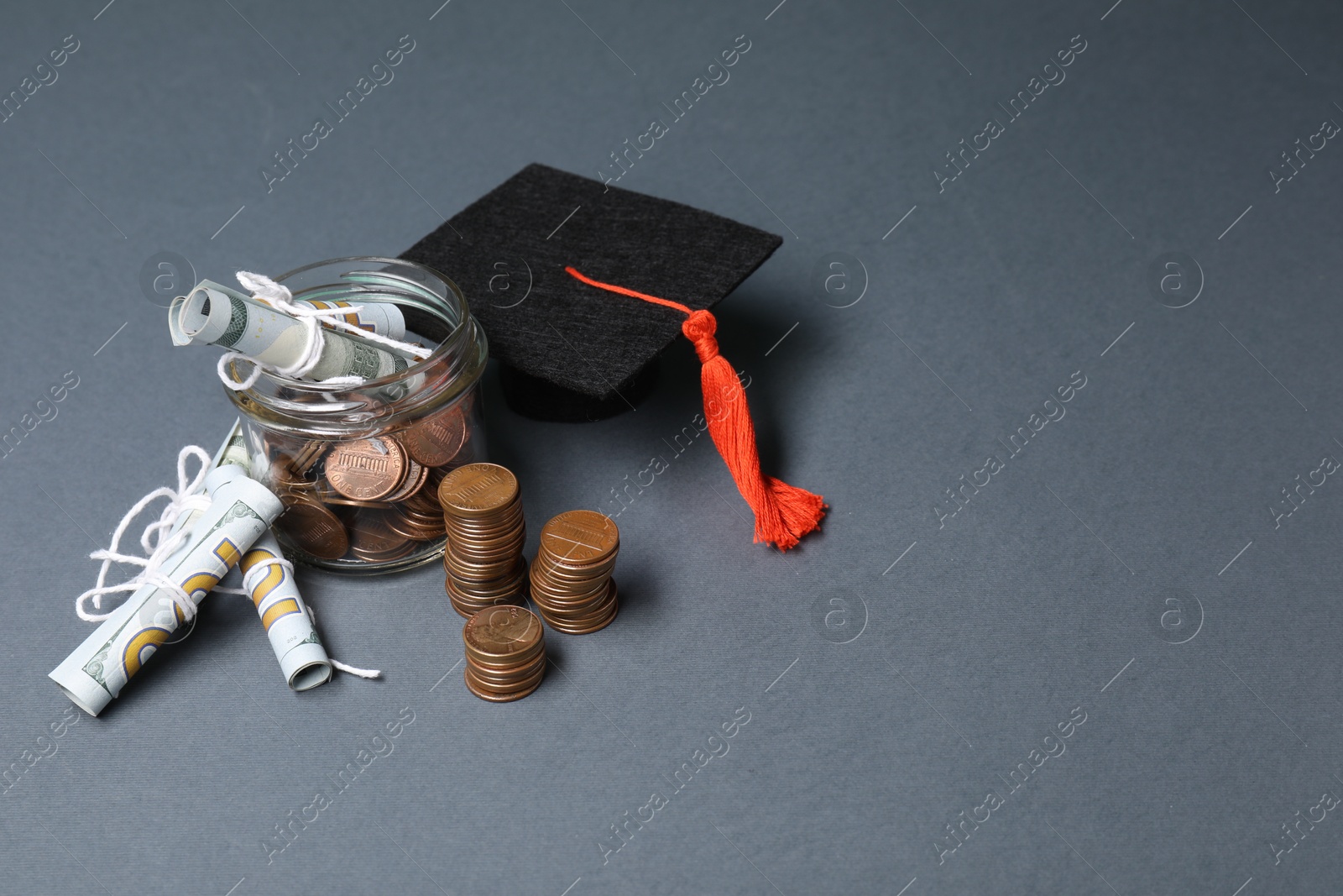 Photo of Dollar banknotes, coins and graduate hat on grey table, space for text. Tuition payment