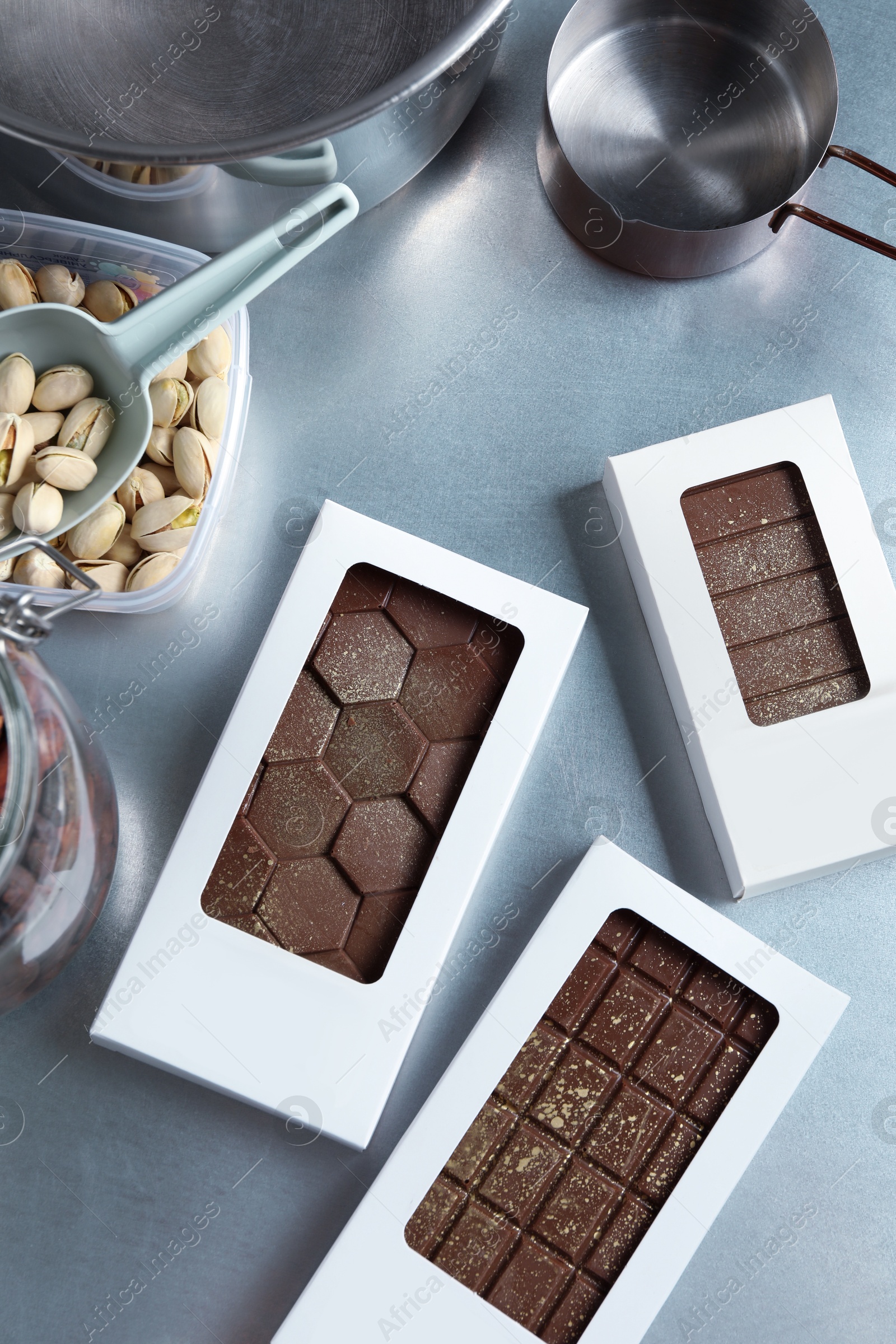 Photo of Different tasty Dubai chocolate bars in packages with pistachios and knafeh on grey table, flat lay