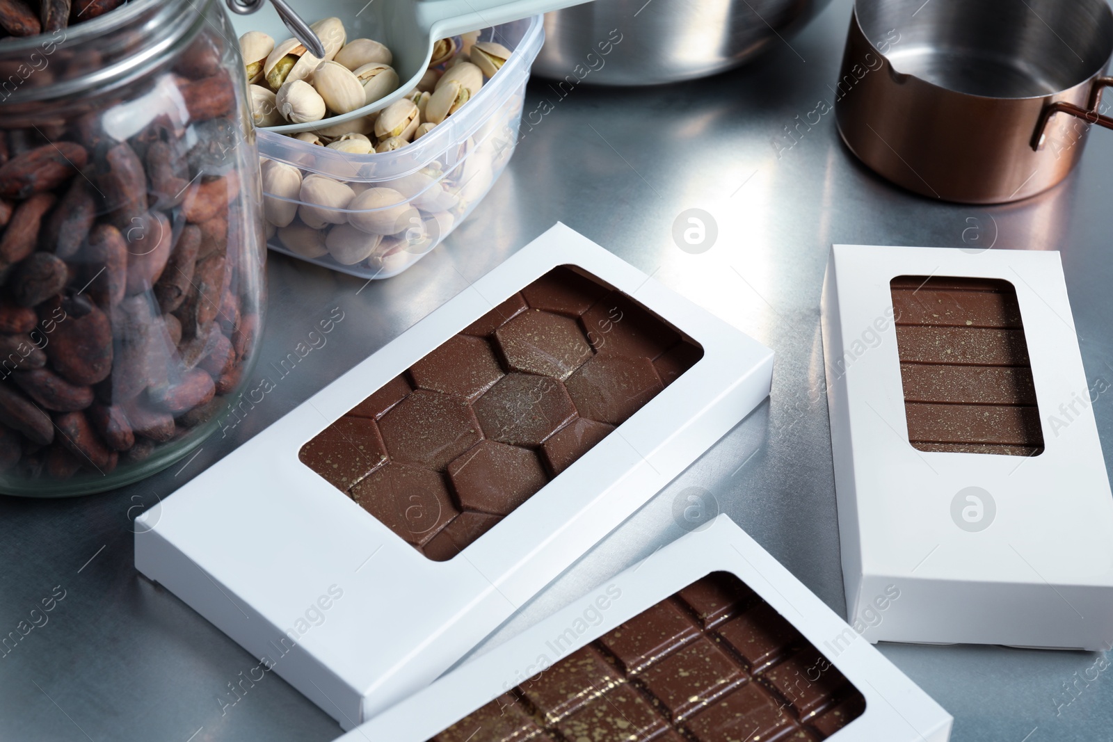 Photo of Different tasty Dubai chocolate bars in packages with pistachios, knafeh and cocoa beans on grey table, closeup. Space for text