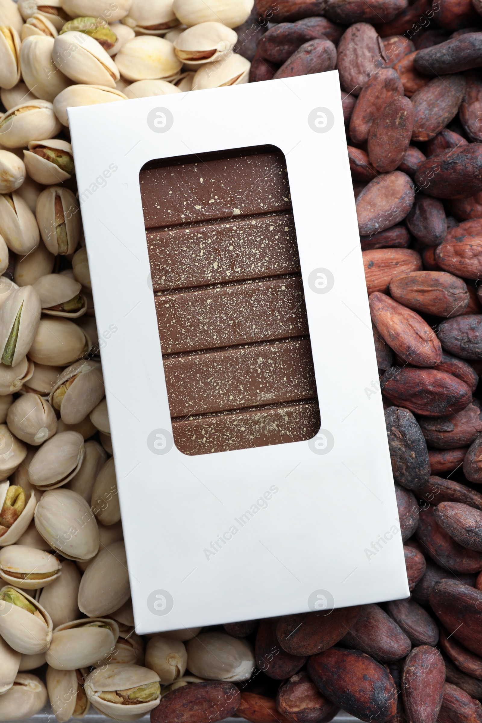 Photo of Tasty Dubai chocolate bar with knafeh in package on pistachios and cocoa beans, top view. Space for text