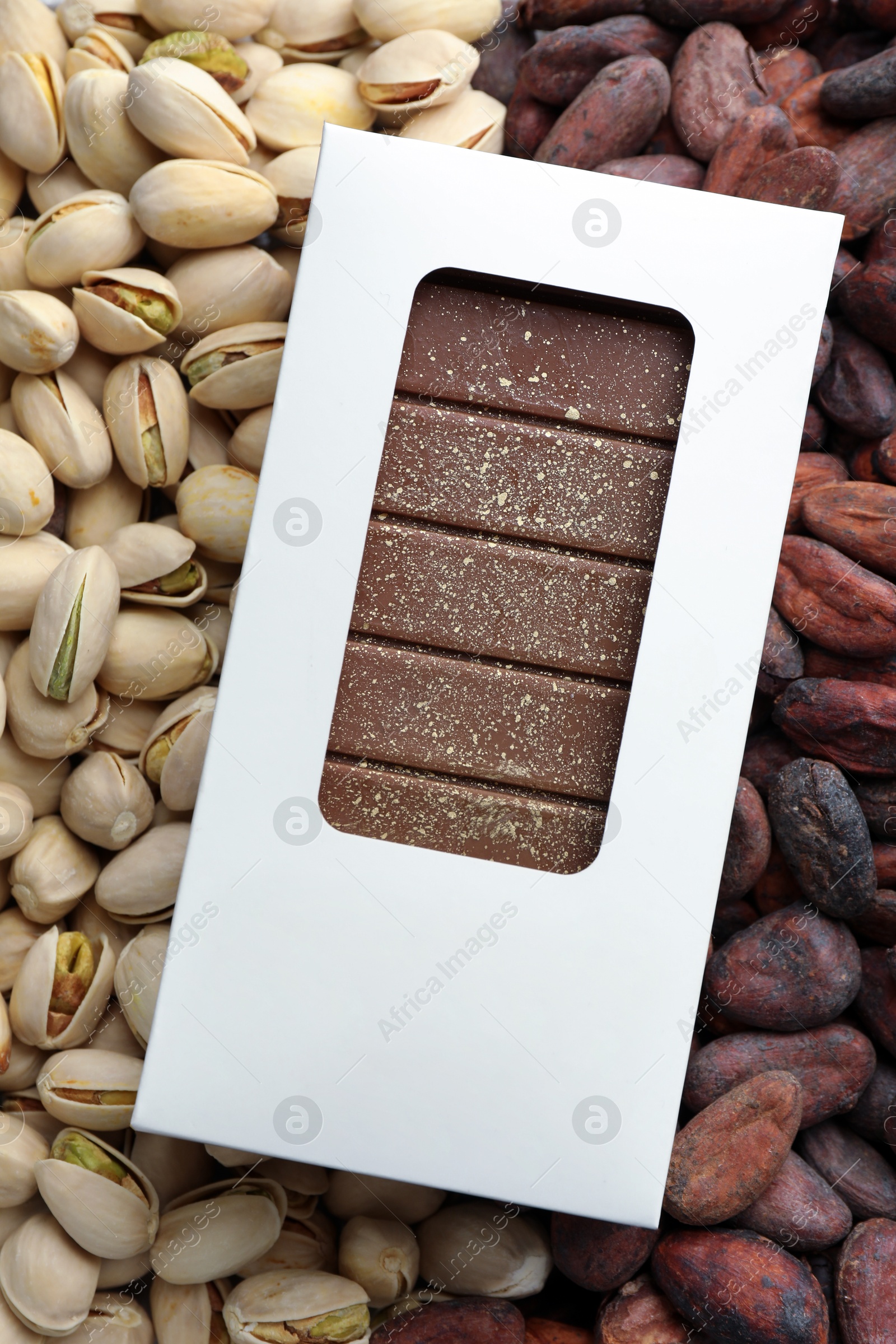 Photo of Tasty Dubai chocolate bar with knafeh in package on pistachios and cocoa beans, top view. Space for text