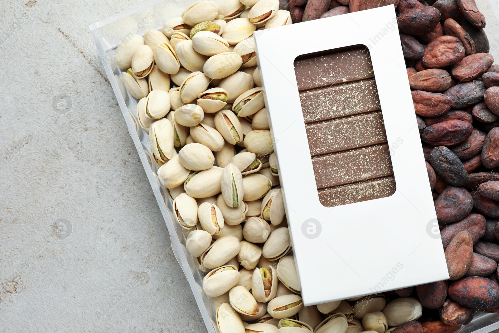 Photo of Tasty Dubai chocolate bar with knafeh in package, pistachios and cocoa beans on textured table, top view. Space for text