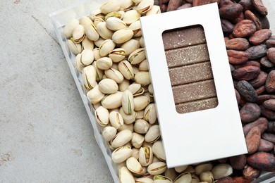 Photo of Tasty Dubai chocolate bar with knafeh in package, pistachios and cocoa beans on textured table, top view. Space for text