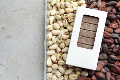 Tasty Dubai chocolate bar with knafeh in package, pistachios and cocoa beans on textured table, top view. Space for text