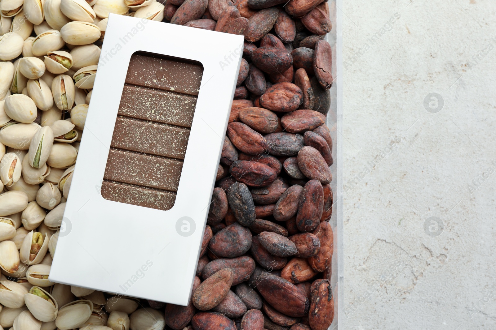 Photo of Tasty Dubai chocolate bar with knafeh in package, pistachios and cocoa beans on textured table, top view. Space for text