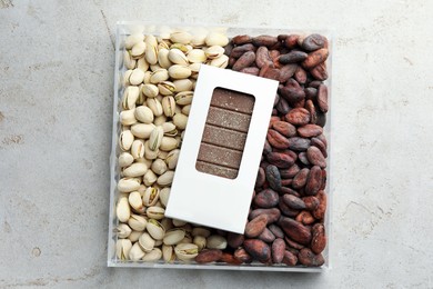 Photo of Tasty Dubai chocolate bar with knafeh in package, pistachios and cocoa beans on textured table, top view. Space for text