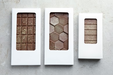 Different tasty Dubai chocolate bars in packages with pistachios and knafeh on textured table, flat lay