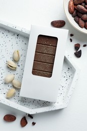 Tasty Dubai chocolate bar in package with pistachios, knafeh and cocoa beans on white table, flat lay. Space for text