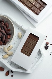 Tasty Dubai chocolate bar in package with pistachios, knafeh and cocoa beans on white table, flat lay. Space for text